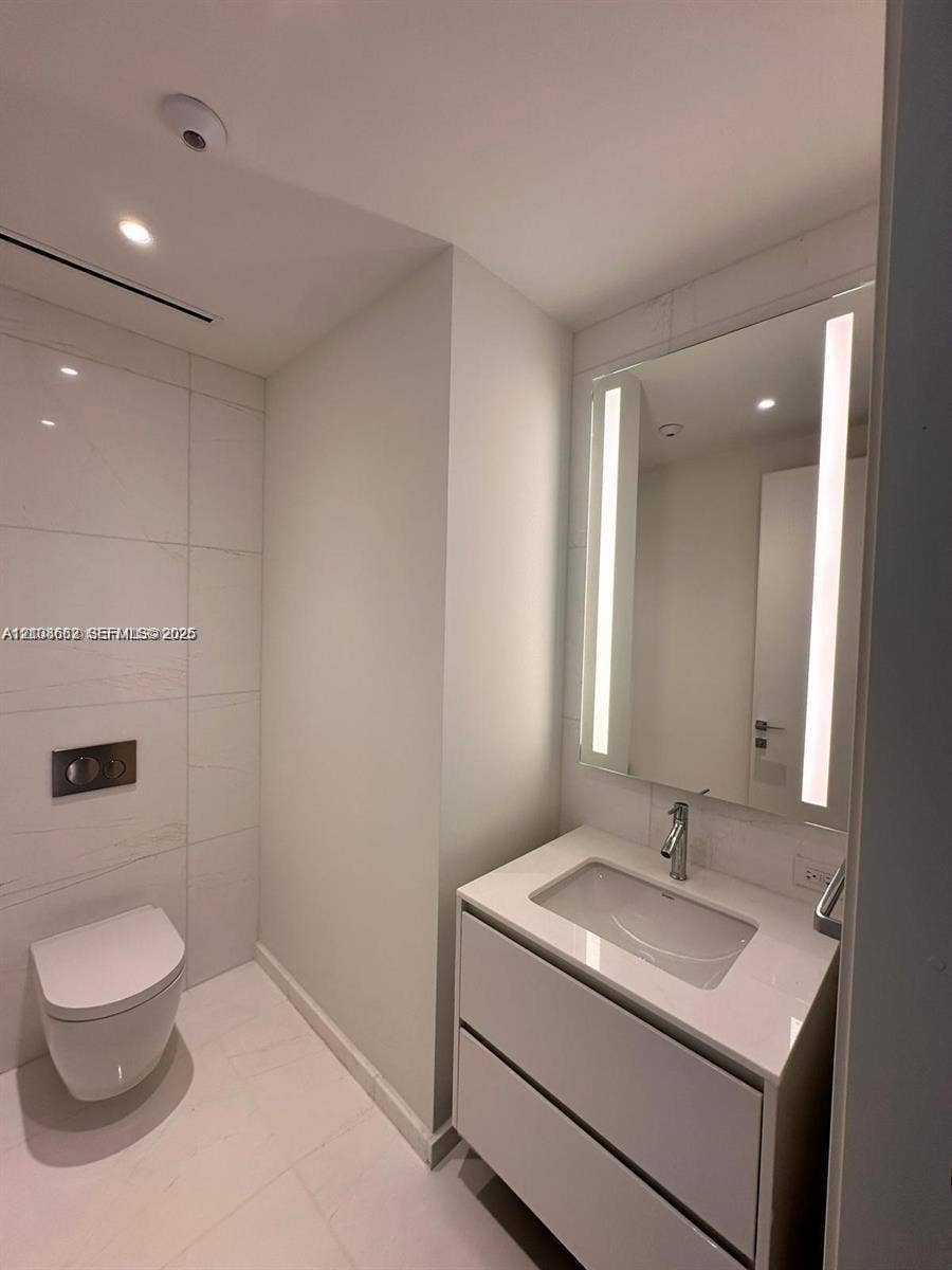 300 Biscayne Boulevard, #2709W, Miami, Miami, FL 33131 Modern bathroom featuring a wall-mounted toilet, floating vanity with a stone-finish countertop, integrated under-mount sink, chrome fixtures, and a vertical LED-backlit mirror