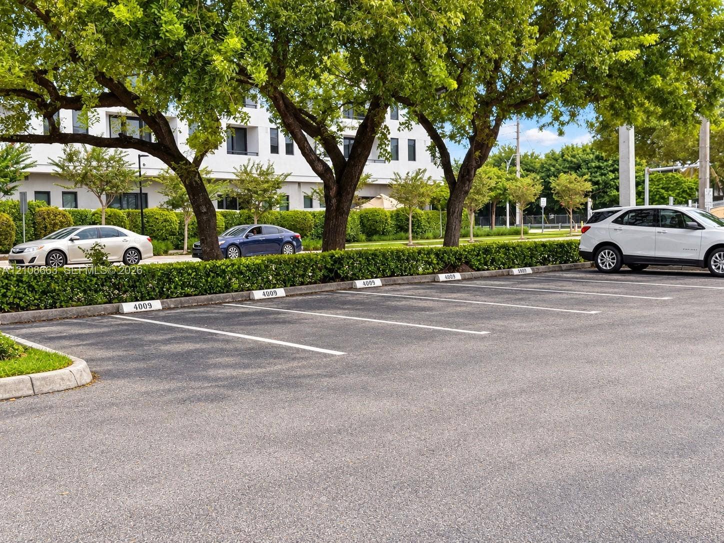 Doral, Doral, FL 33166 Paved surface parking area with numbered concrete wheel stops, bordered by manicured hedges and mature trees