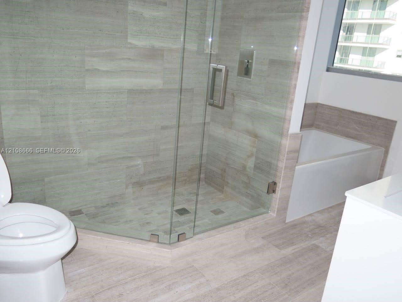 1300 Brickell Bay Drive, #3506, Miami, FL 33131 Walk-in glass-enclosed shower featuring large-format stone-finish tile surround and floor, deep soaking tub with tile surround, and neutral wood-finish flooring