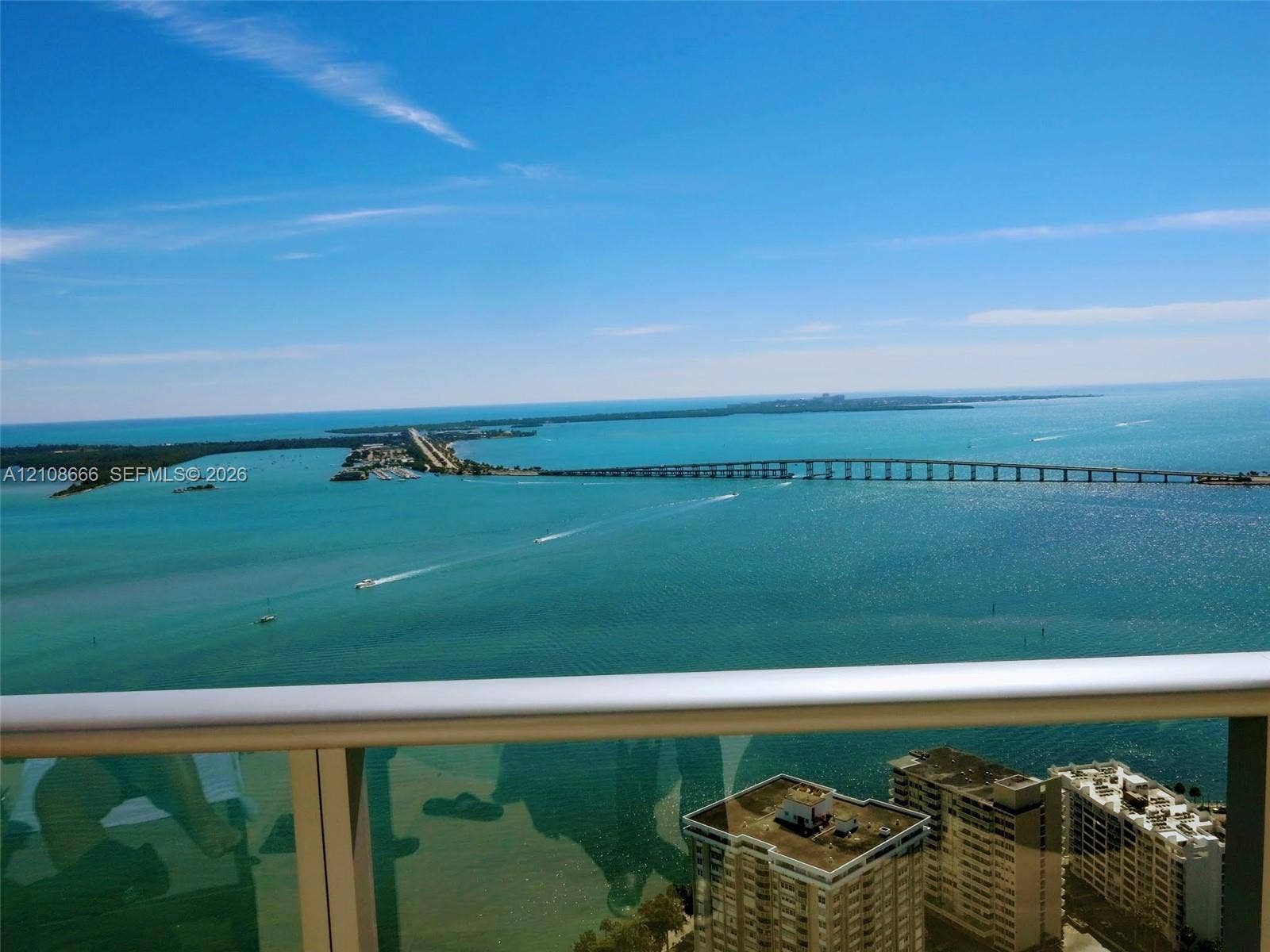 1300 Brickell Bay Drive, #3506, Miami, FL 33131 High-rise balcony featuring a metal railing with glass panels, showcasing panoramic coastal scenery, open water, and a bridge