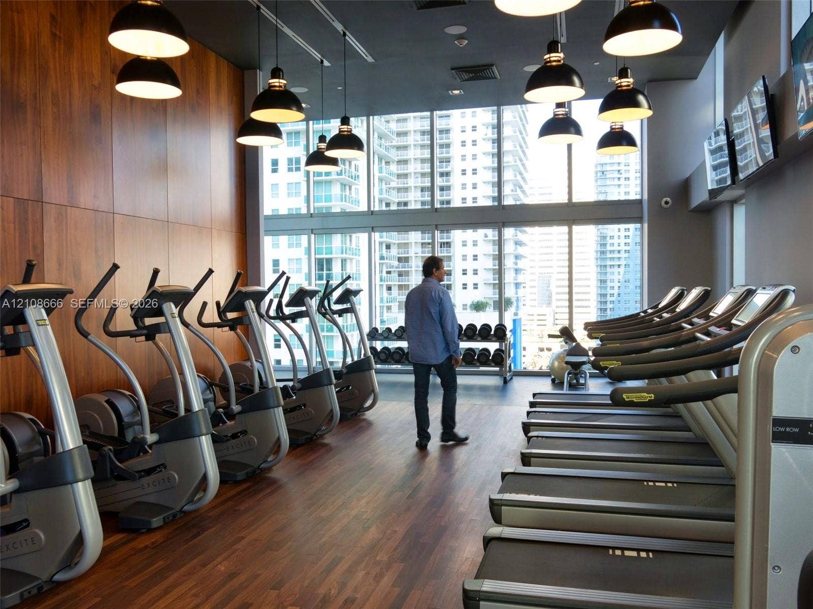 1300 Brickell Bay Drive, #3506, Miami, FL 33131 Fitness center featuring floor-to-ceiling windows, wood-finish flooring, wood-paneled accent wall, and industrial-style pendant lighting
