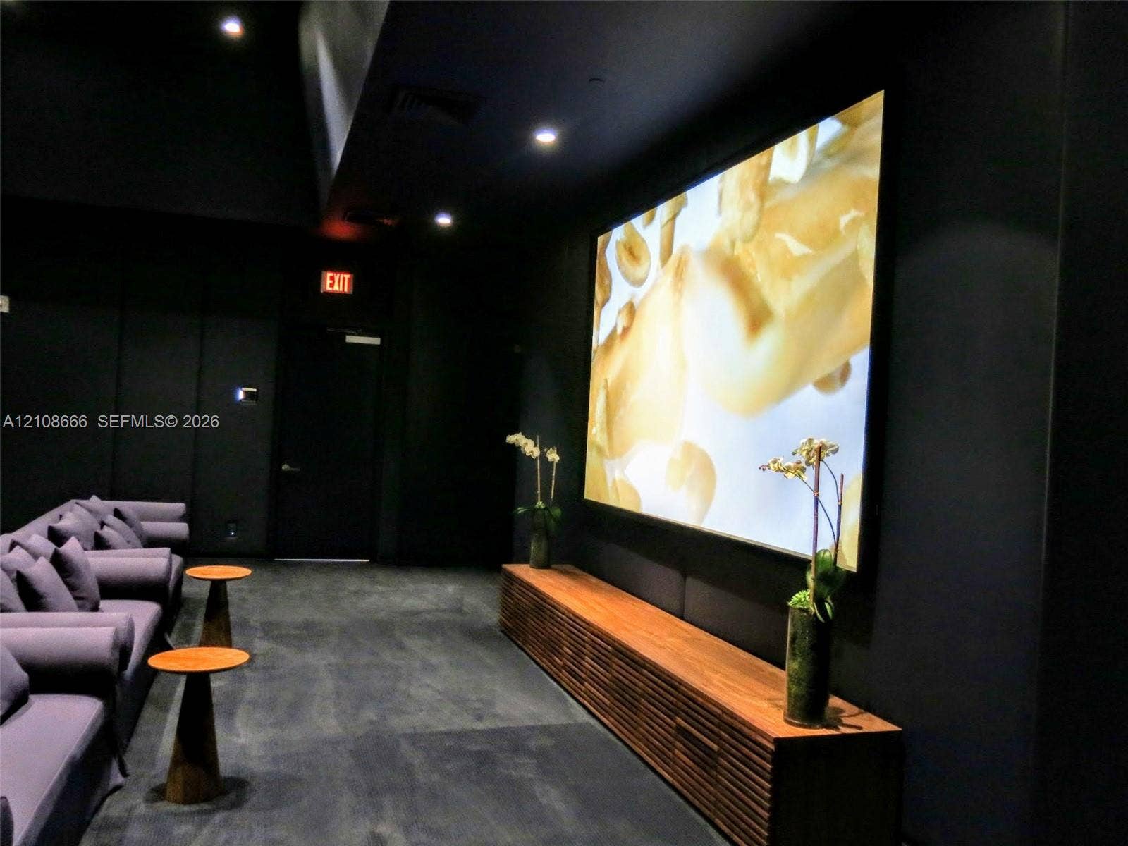 1300 Brickell Bay Drive, #3506, Miami, FL 33131 Media room featuring dark wall finishes, a large-format mounted screen, and a custom slatted wood-finish media console with recessed ceiling lighting