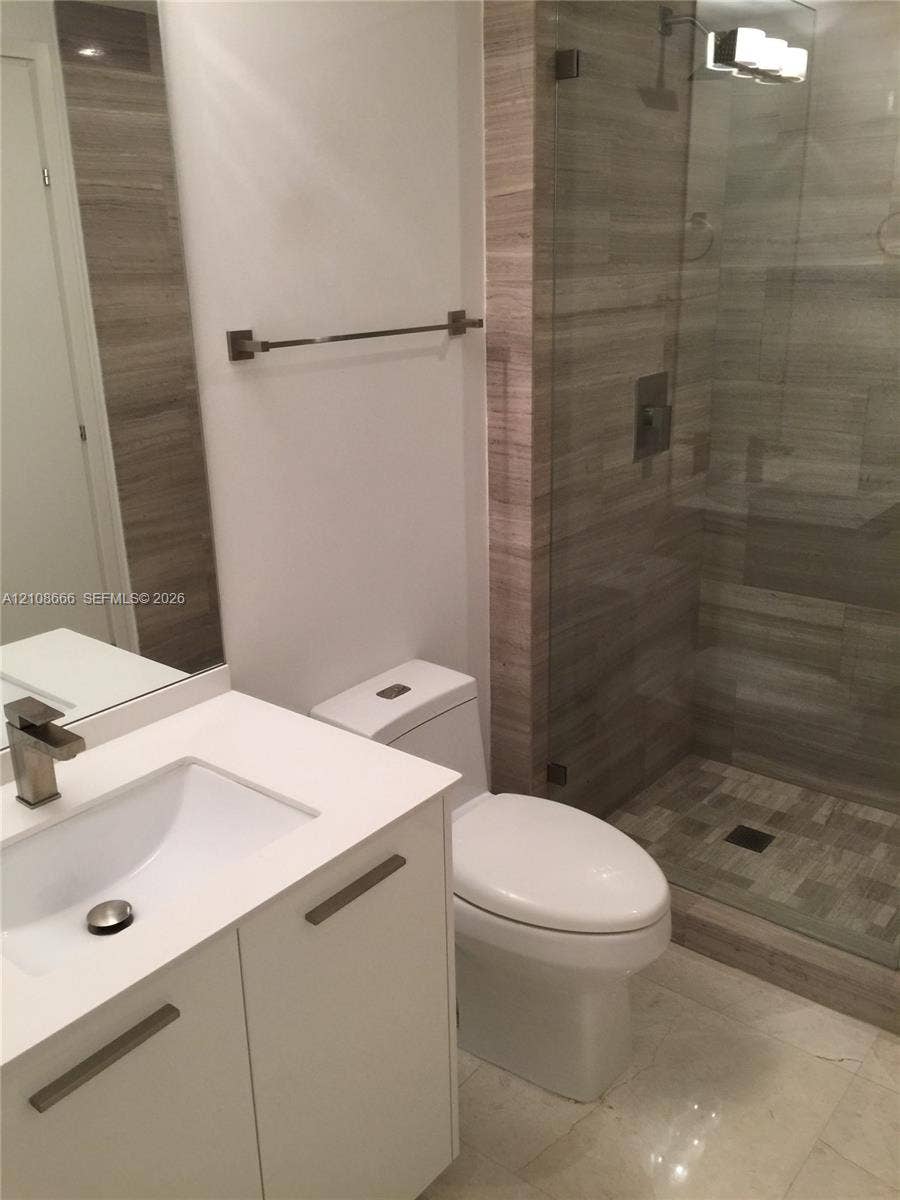 1300 Brickell Bay Drive, #3506, Miami, FL 33131 Modern bathroom featuring a white vanity with a rectangular basin, metallic single-handle faucet, glass-enclosed shower with tiled surround, and integrated lighting