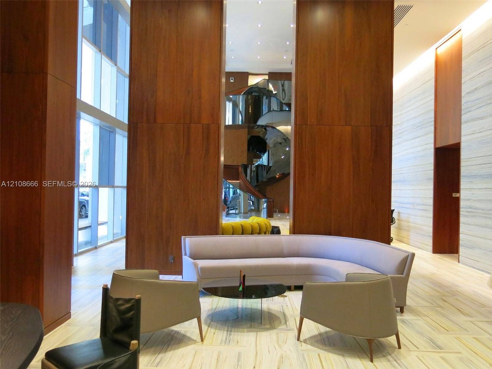 1300 Brickell Bay Drive, #3506, Miami, FL 33131 Grand foyer featuring double-height ceilings, floor-to-ceiling wood paneling, large-format stone flooring, integrated recessed lighting, and a sculptural spiral staircase