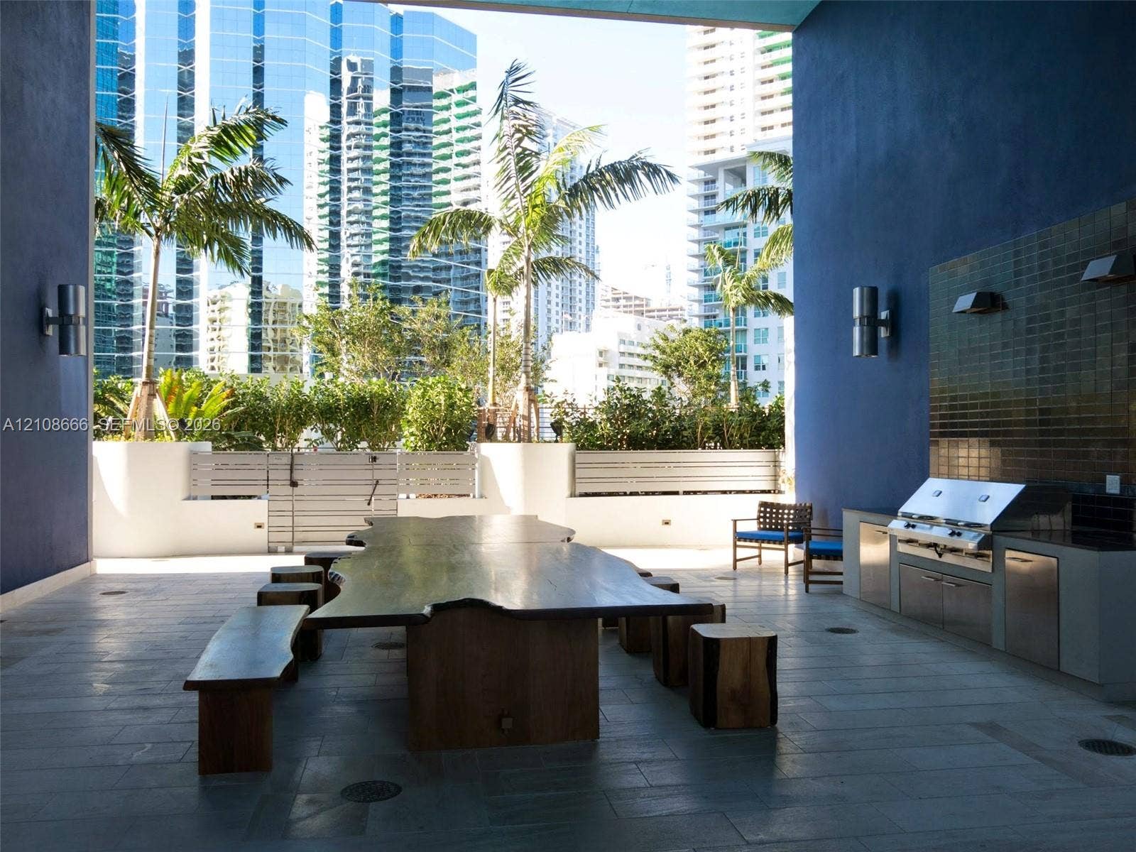 1300 Brickell Bay Drive, #3506, Miami, FL 33131 Covered outdoor terrace featuring a built-in stainless steel grill, stone tile flooring, wall-mounted cylinder sconces, and a tile backsplash