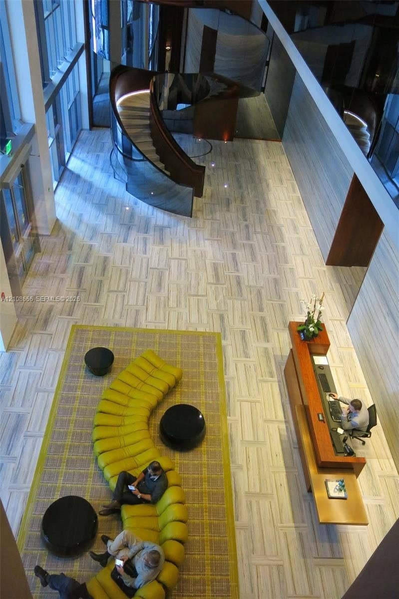 1300 Brickell Bay Drive, #3506, Miami, FL 33131 Double-height ceiling, sculptural spiral staircase with glass railing, stone tile flooring, and integrated wood-finish reception desk