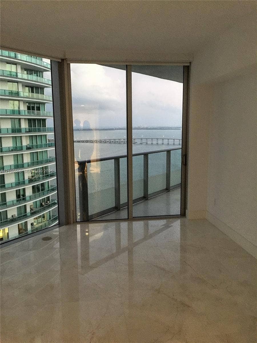1300 Brickell Bay Drive, #3506, Miami, FL 33131 Floor-to-ceiling glass sliding doors, stone-finish flooring, and a private balcony featuring a glass railing and water backdrop