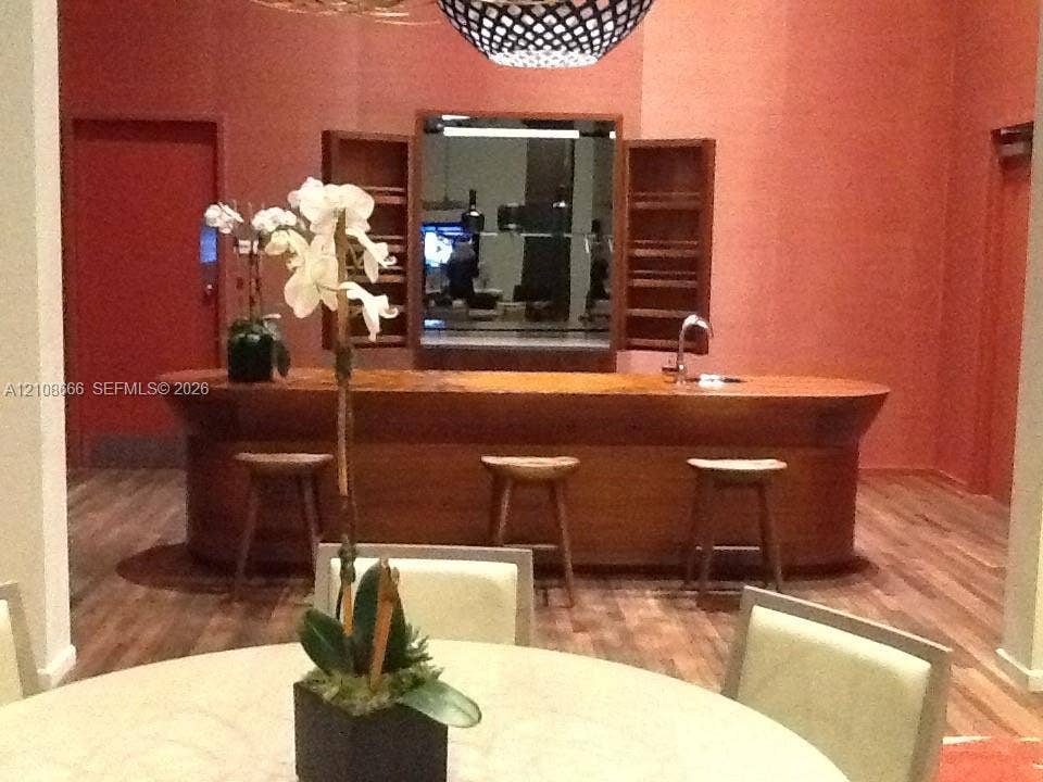 1300 Brickell Bay Drive, #3506, Miami, FL 33131 Custom wood-finished bar featuring a curved design, built-in shelving, a stainless steel sink, and wood-finish flooring