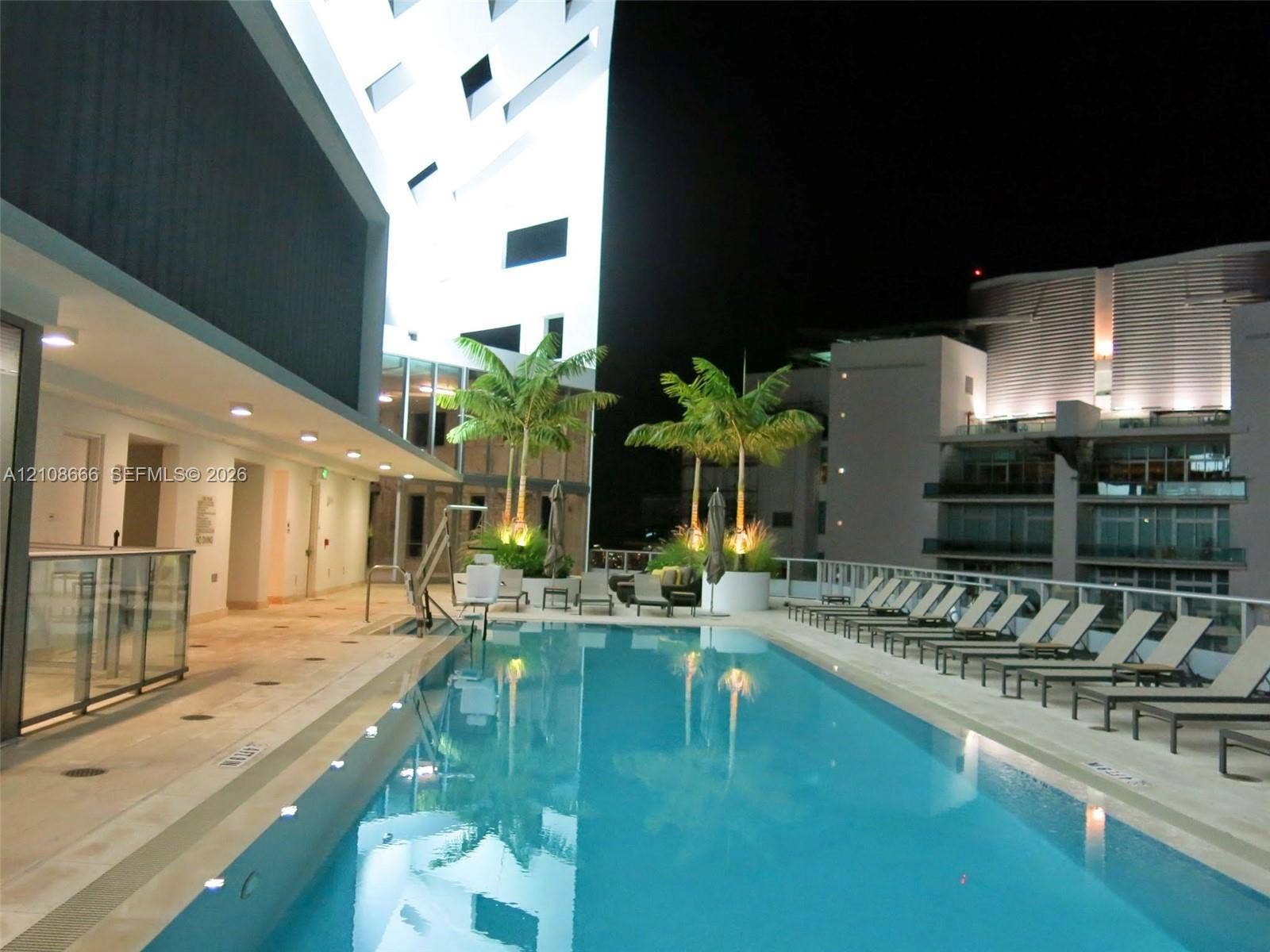 1300 Brickell Bay Drive, #3506, Miami, FL 33131 Rectangular swimming pool featuring a light-toned deck, integrated pool lift, recessed lighting, and palm tree planters