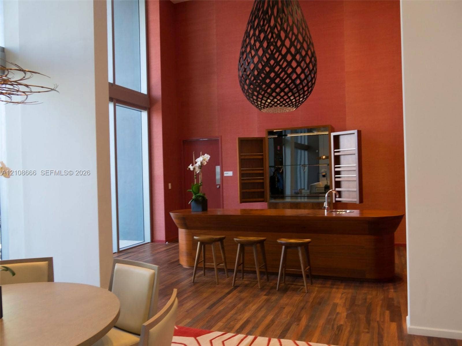 1300 Brickell Bay Drive, #3506, Miami, FL 33131 Double-height windows, wood-finish flooring, custom wood-paneled bar with integrated sink, and an oversized decorative pendant light fixture