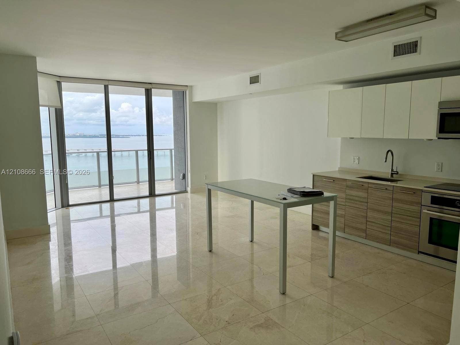 1300 Brickell Bay Drive, #3506, Miami, FL 33131 Open-concept kitchen featuring two-tone cabinetry, stone-finish countertops, stainless steel appliances, polished stone flooring, and expansive floor-to-ceiling glass panel doors