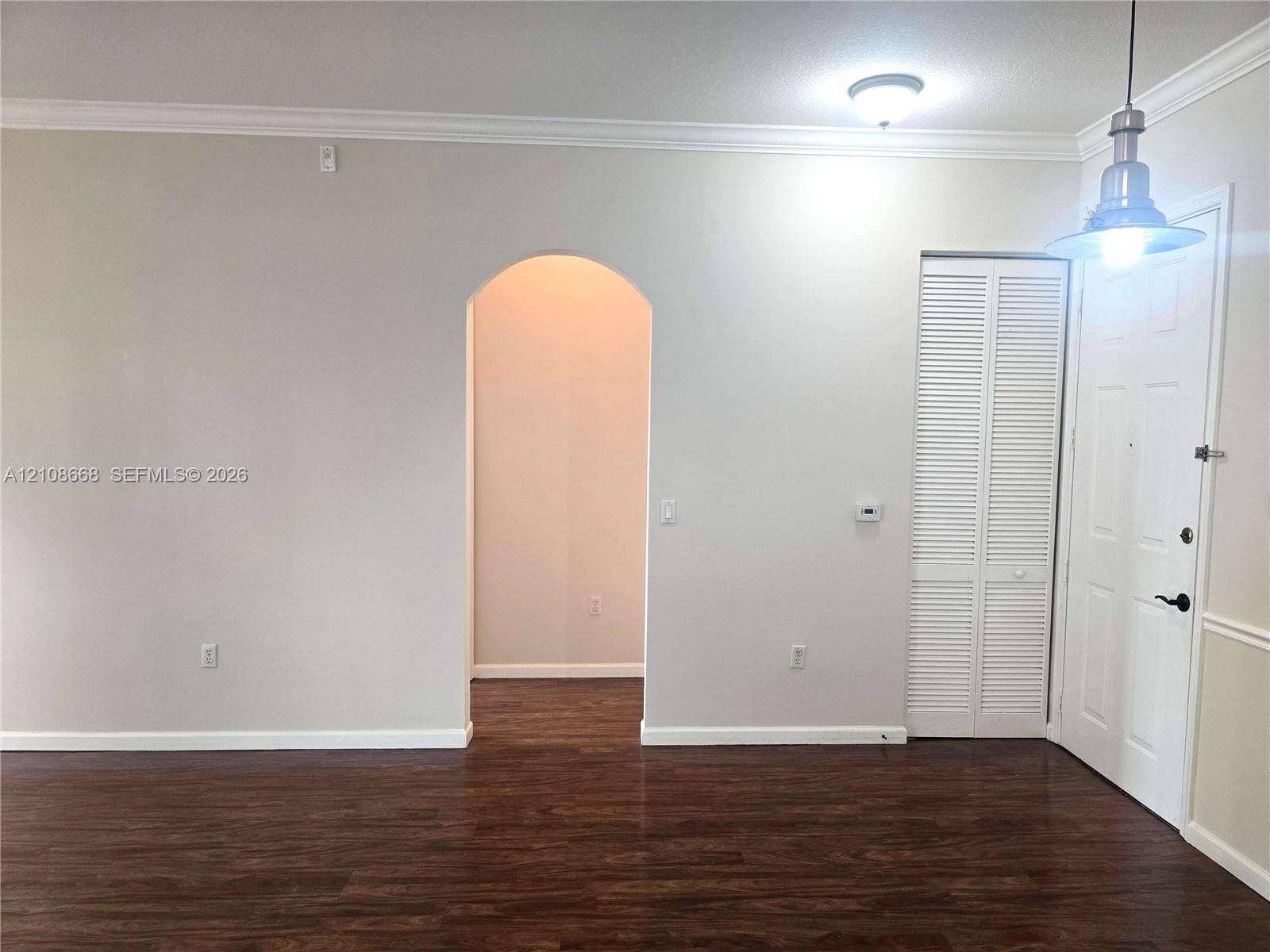 4508 SW 160th Avenue, #734, Miramar, Miramar, FL 33027 Interior space featuring wood-finish flooring, an arched architectural opening, crown molding, a louvered bi-fold closet door, and a metal pendant light fixture