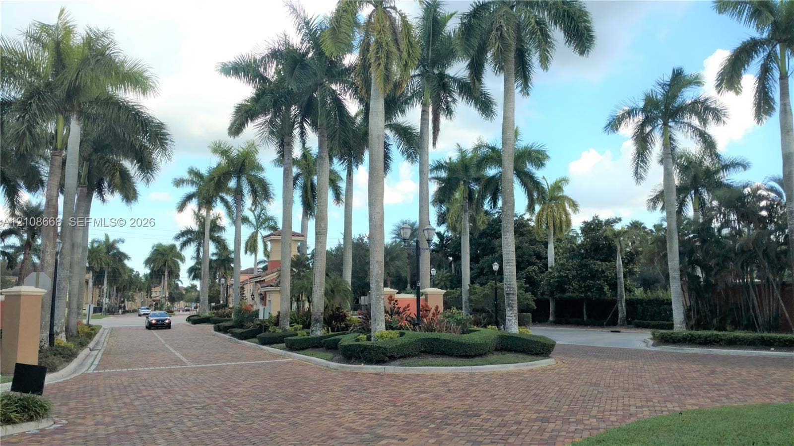 4508 SW 160th Avenue, #734, Miramar, Miramar, FL 33027 Paver driveway and road featuring mature palm trees, manicured landscape hedging, and decorative street lighting