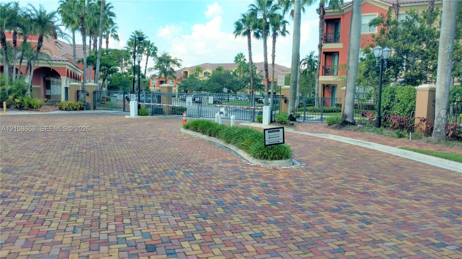 4508 SW 160th Avenue, #734, Miramar, Miramar, FL 33027 Gated community entry featuring paver-stone driveway, metal security gate, and mature palm trees