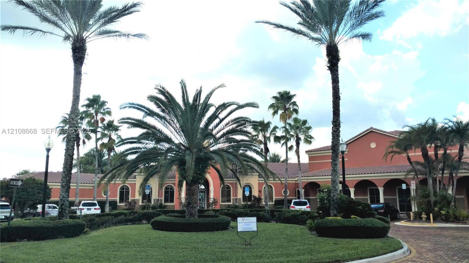 4508 SW 160th Avenue, #734, Miramar, Miramar, FL 33027 Stucco exterior featuring arched breezeways, a terra-cotta tile roof, mature palm trees, manicured landscaping, and a brick-paver circular driveway