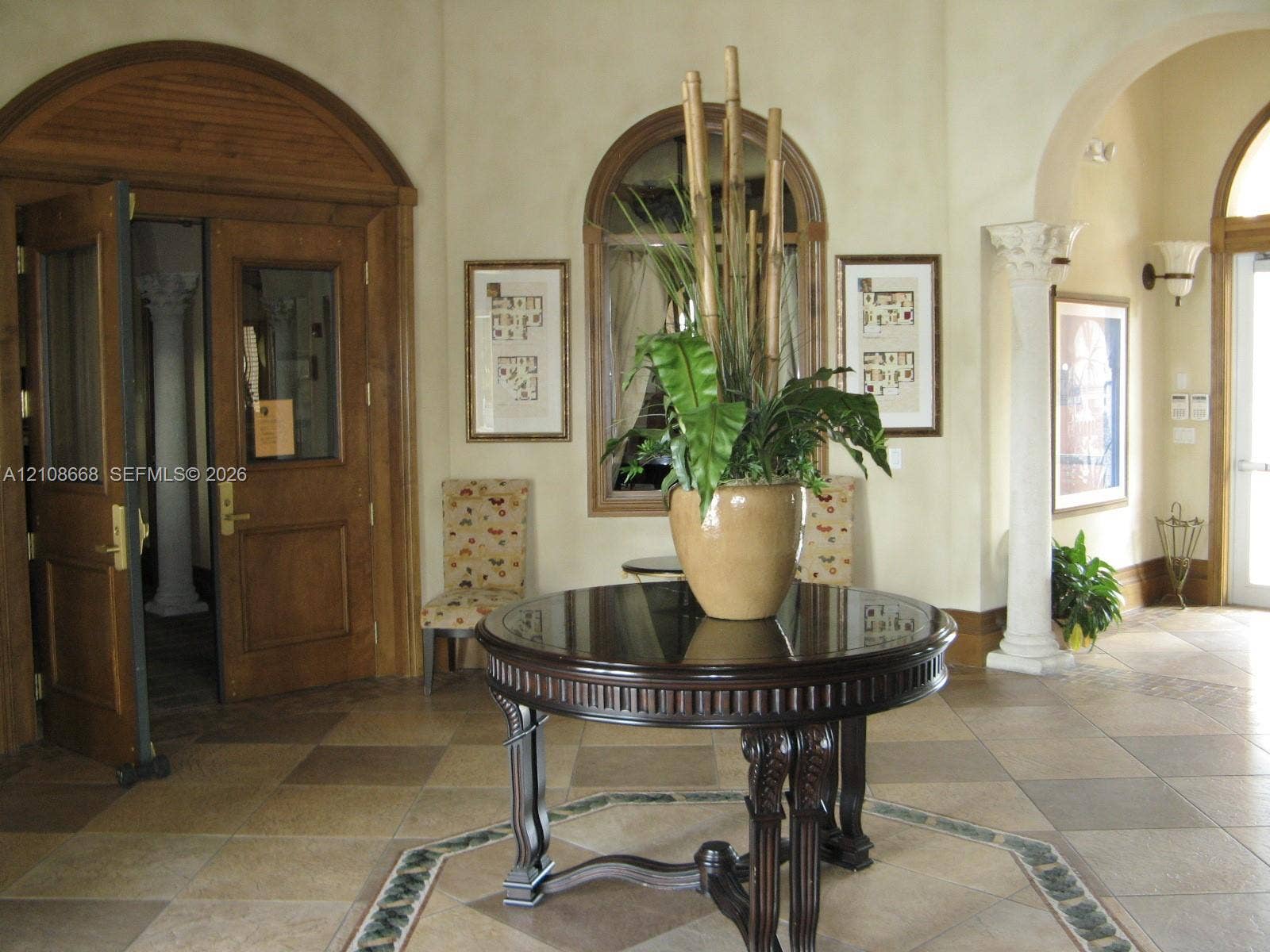 4508 SW 160th Avenue, #734, Miramar, Miramar, FL 33027 Foyer featuring arched wood double doors, decorative column, tile flooring with intricate border inlay, arched window, and wall-mounted sconce lighting