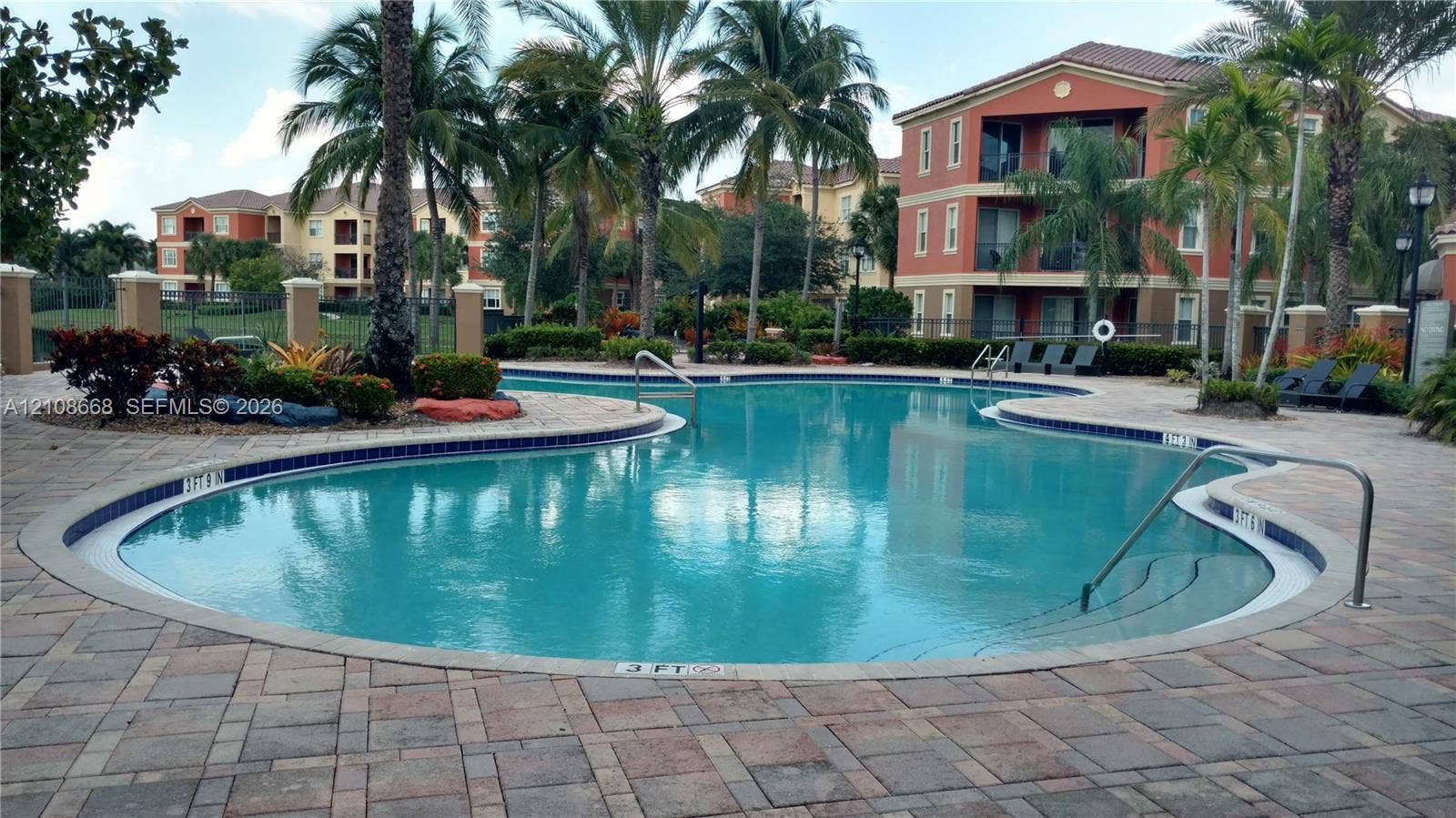 4508 SW 160th Avenue, #734, Miramar, Miramar, FL 33027 Curved swimming pool featuring paved decking, metal handrails, mature palm trees, and multi-story building structures