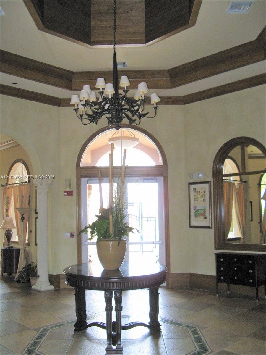 4508 SW 160th Avenue, #734, Miramar, Miramar, FL 33027 Foyer featuring a coffered octagonal ceiling with wood-finish trim, a prominent iron chandelier, arched doorways, tiled flooring with an inlaid decorative border, and a decorative column