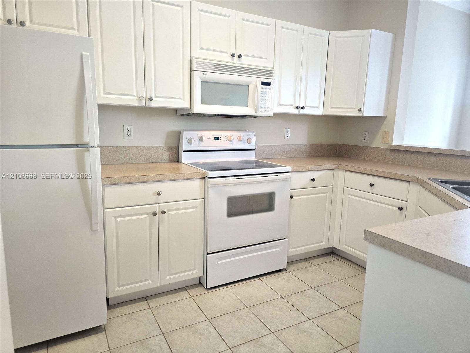 4508 SW 160th Avenue, #734, Miramar, Miramar, FL 33027 Kitchen featuring white shaker-style cabinetry, neutral-toned countertops, tile flooring, and integrated white appliances including a range and microwave