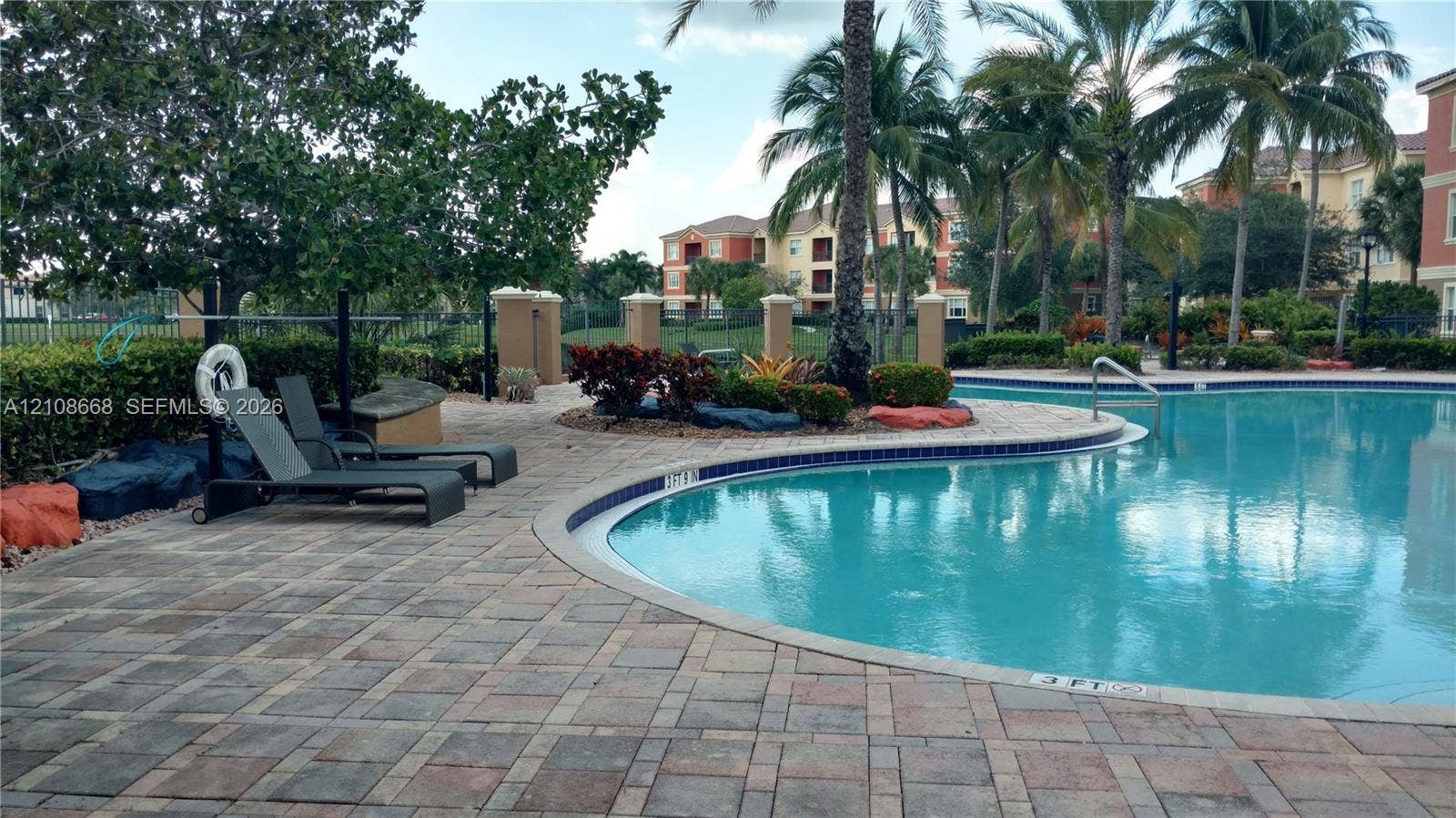 4508 SW 160th Avenue, #734, Miramar, Miramar, FL 33027 Curved swimming pool featuring a paver deck, mature palm trees, integrated landscaping, and decorative boulder accents