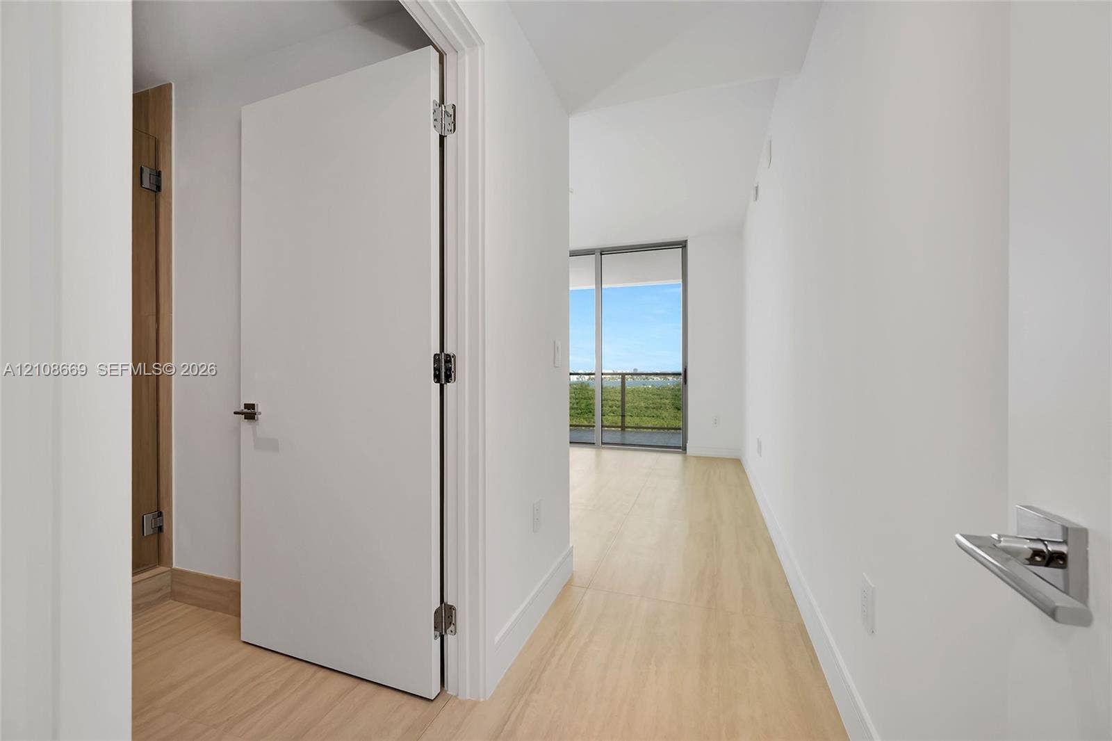 Interior space featuring wood-finish flooring, white walls, flush-panel doors, modern lever-style hardware, and floor-to-ceiling sliding glass doors