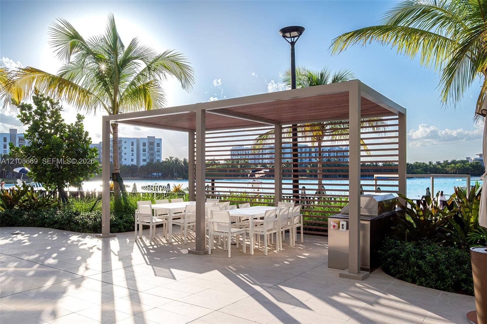 Outdoor patio featuring a covered pergola with horizontal slat privacy screening, light-toned stone tile flooring, and a built-in stainless steel outdoor kitchen station