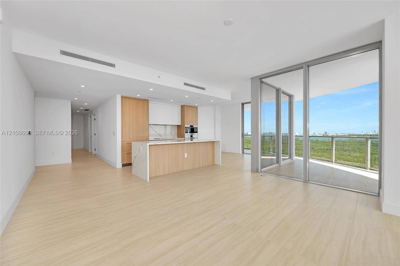 Open-concept interior featuring wood-finish flooring, kitchen island with stone-surface countertop, floor-to-ceiling glass sliding doors, and built-in stainless steel wall oven