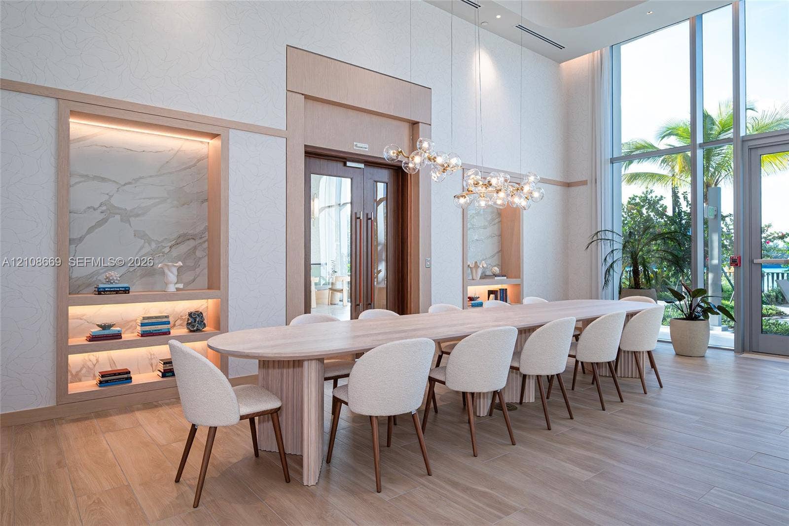 Double-height ceilings with floor-to-ceiling windows, built-in recessed shelving featuring integrated lighting and stone-finish backings, wood-finish tile flooring, and a contemporary multi-globe statement chandelier