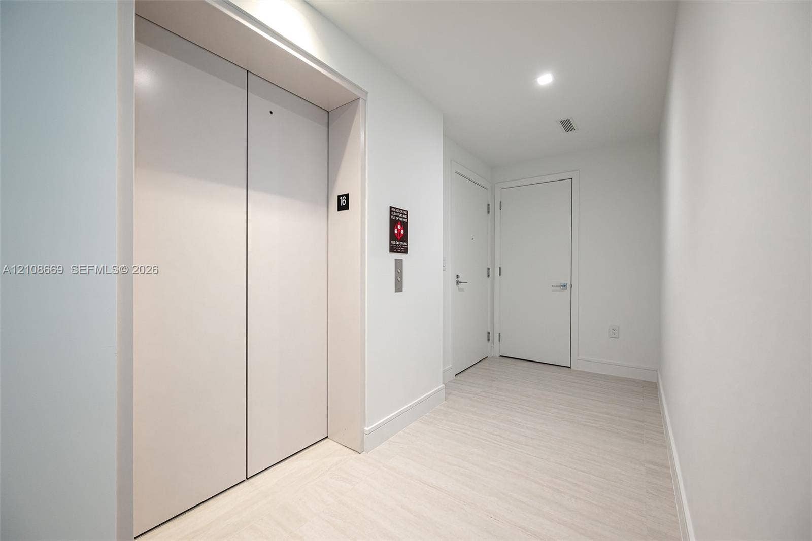 Elevator foyer featuring smooth-finish ceiling with recessed lighting, light-toned wood-finish flooring, and minimalist white interior doors