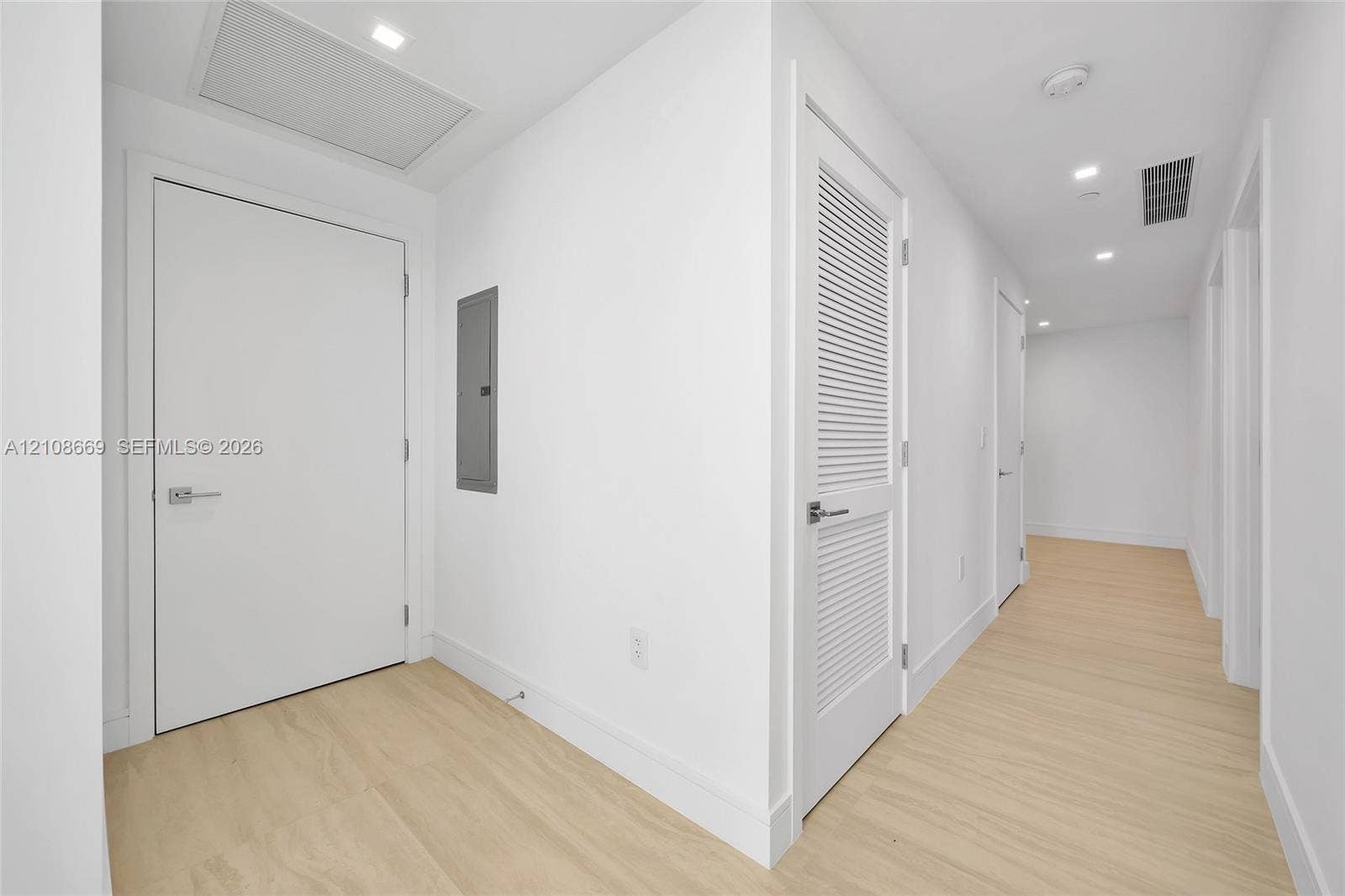 Hallway featuring light-toned wood-finish flooring, recessed ceiling lighting, and crisp white walls