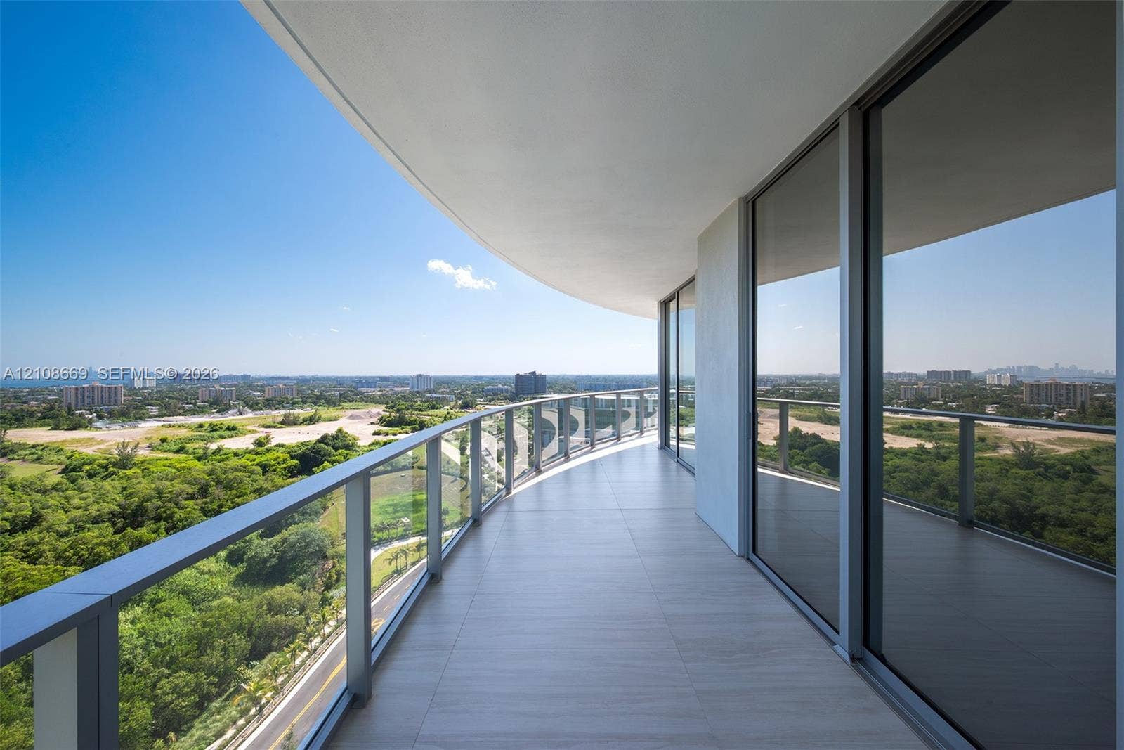 Curved balcony featuring large-format tile flooring, a glass and metal railing, and floor-to-ceiling sliding glass doors