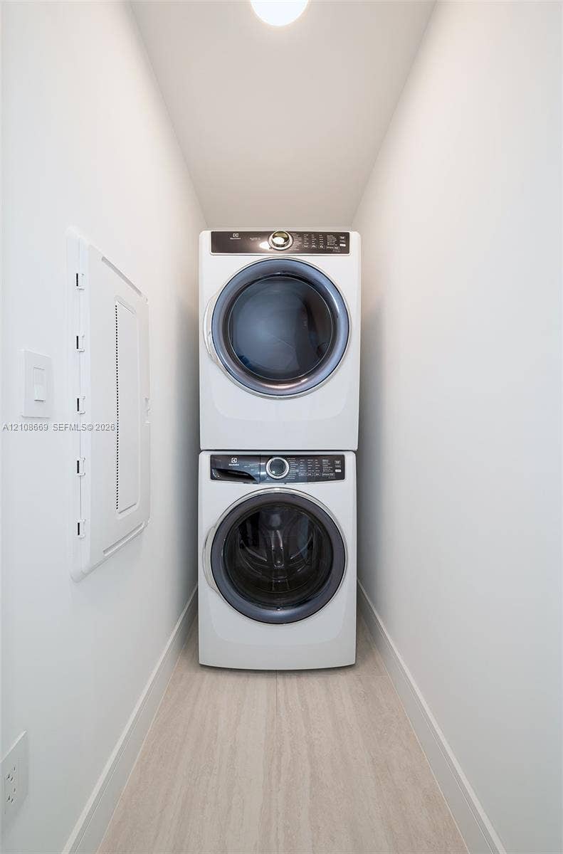 Dedicated laundry alcove featuring a stacked white front-loading washer and dryer set on light-toned wood-finish flooring