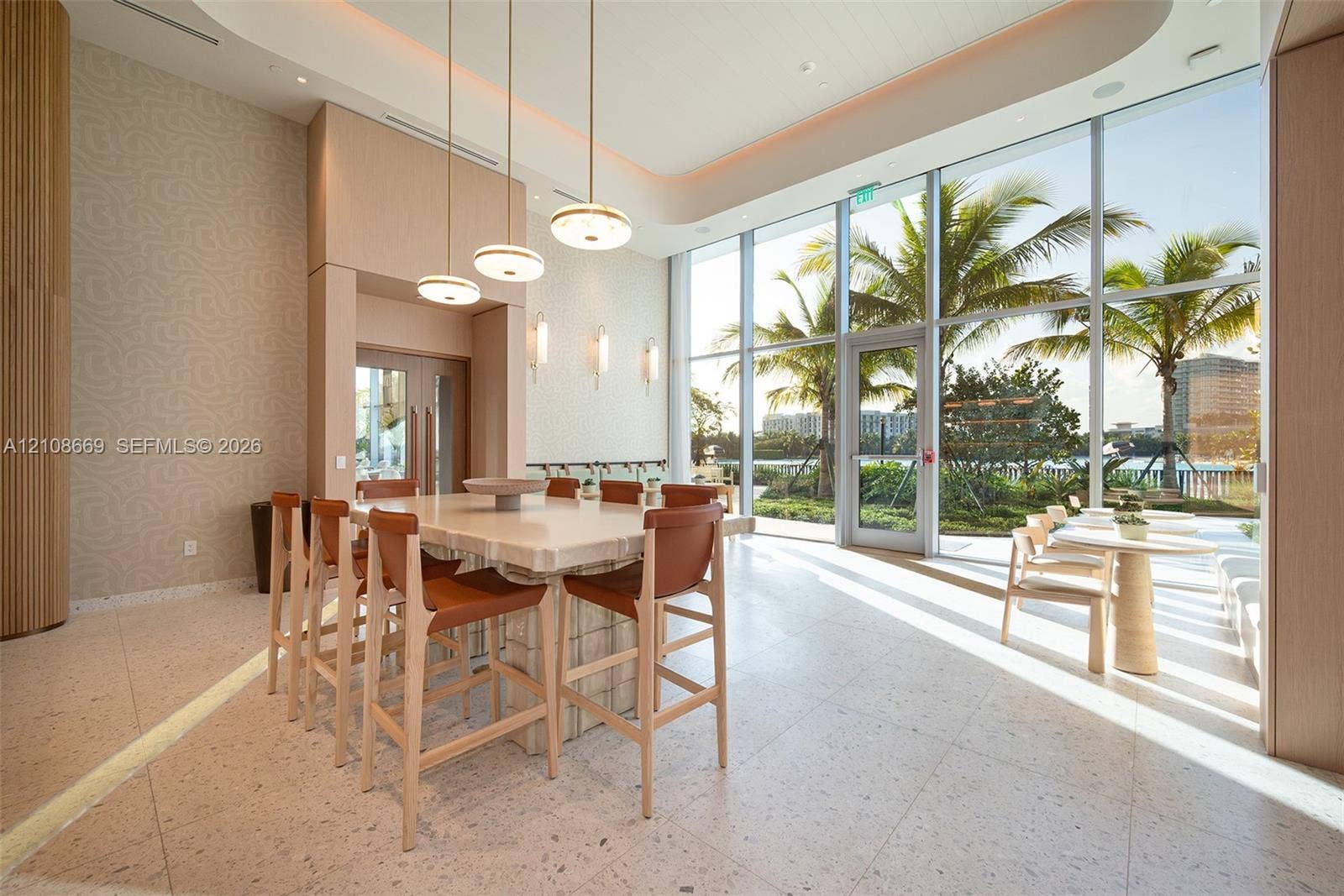 Expansive common area featuring floor-to-ceiling glass windows, recessed tray ceiling lighting, stone-top island with integrated seating, and polished stone flooring