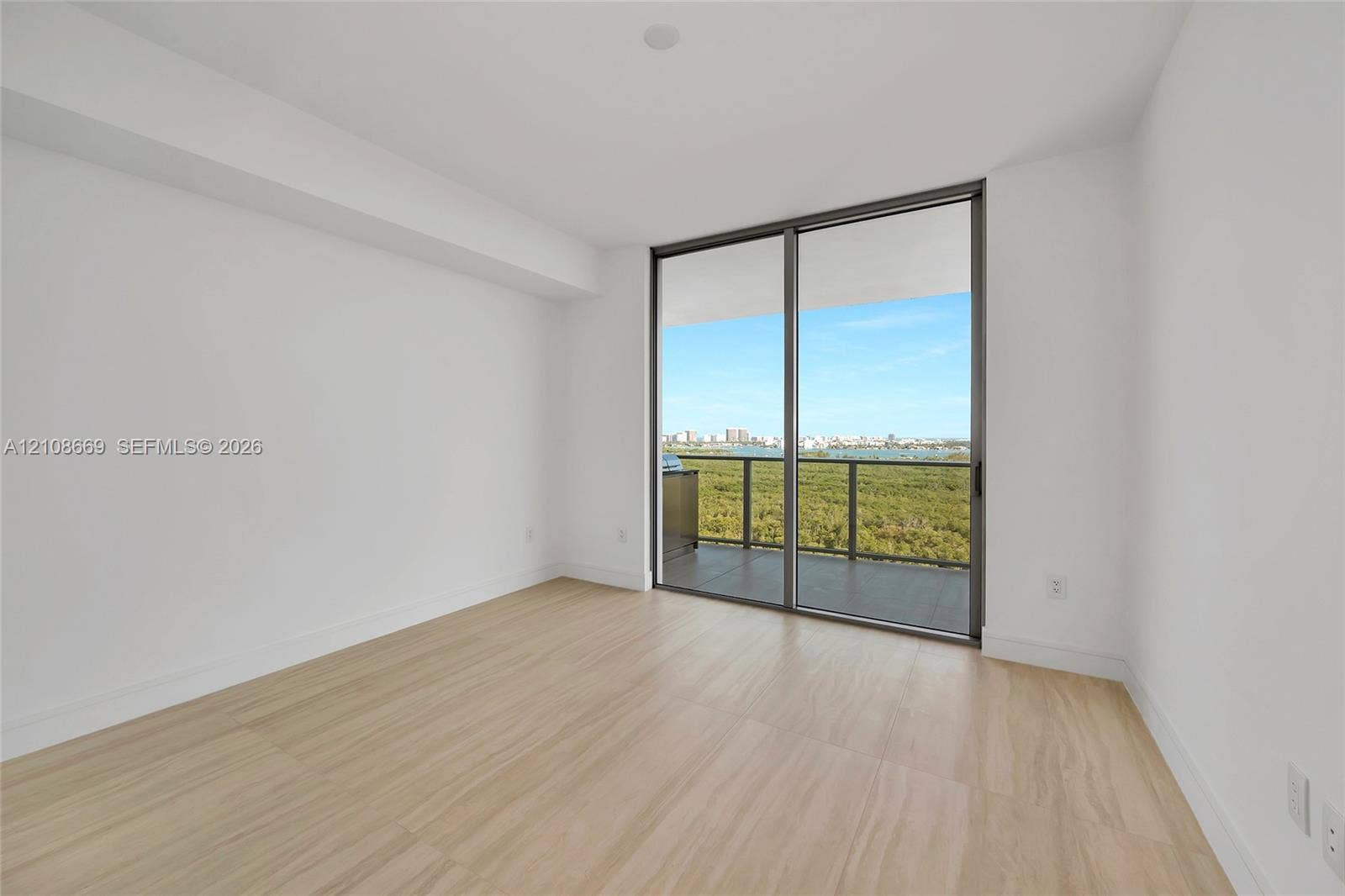 Neutral-toned interior featuring wood-finish flooring, full-height floor-to-ceiling glass sliding doors, and a private balcony with water and coastal scenery
