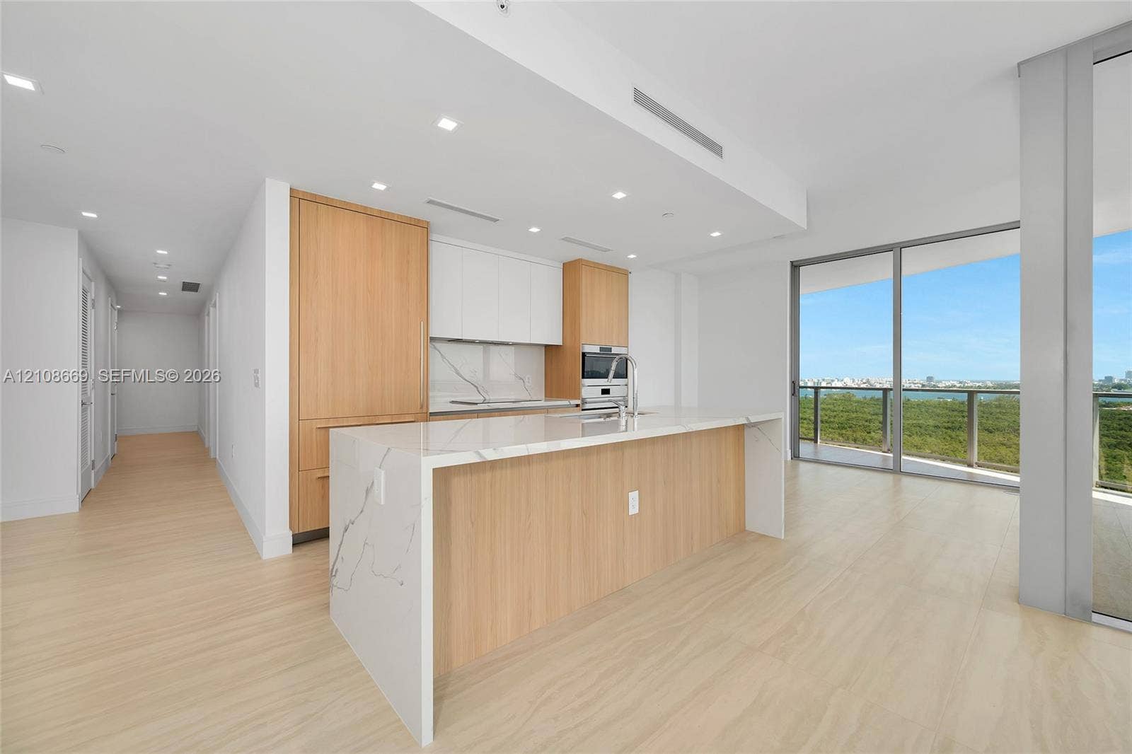 Kitchen featuring wood-finish cabinetry, stone-surfaced waterfall island, integrated appliances, recessed lighting, and floor-to-ceiling glass sliding doors