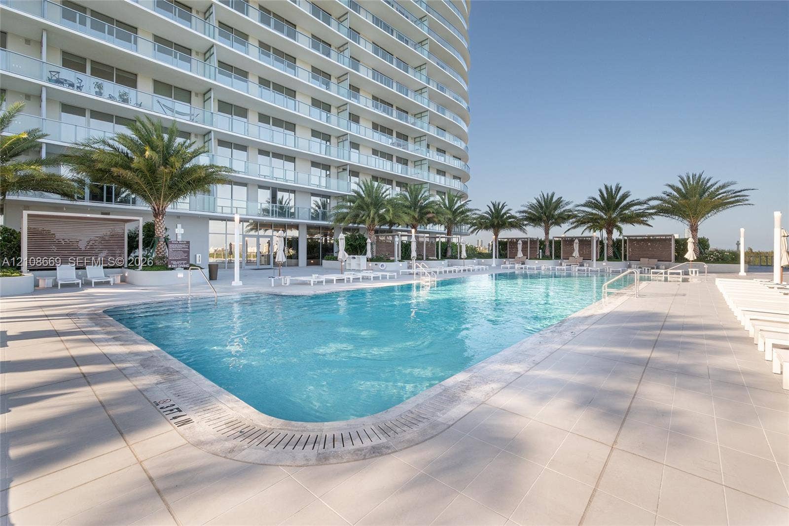 Swimming pool with ceramic tile surround, palm tree landscaping, and cabana structures