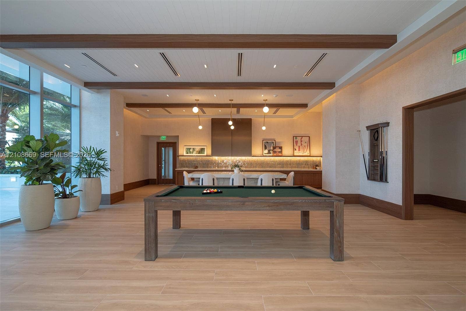 Spacious room featuring wood-finish flooring, recessed ceiling lighting with wooden beams, floor-to-ceiling windows, and built-in cabinetry with under-cabinet lighting