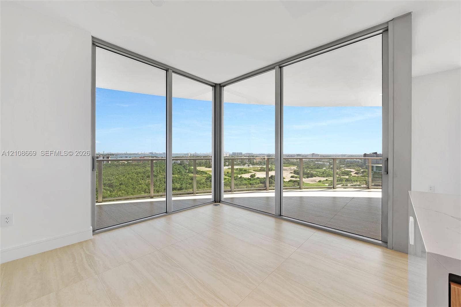 Floor-to-ceiling corner glass windows, expansive wrap-around balcony, neutral large-format tile flooring, and metallic railings