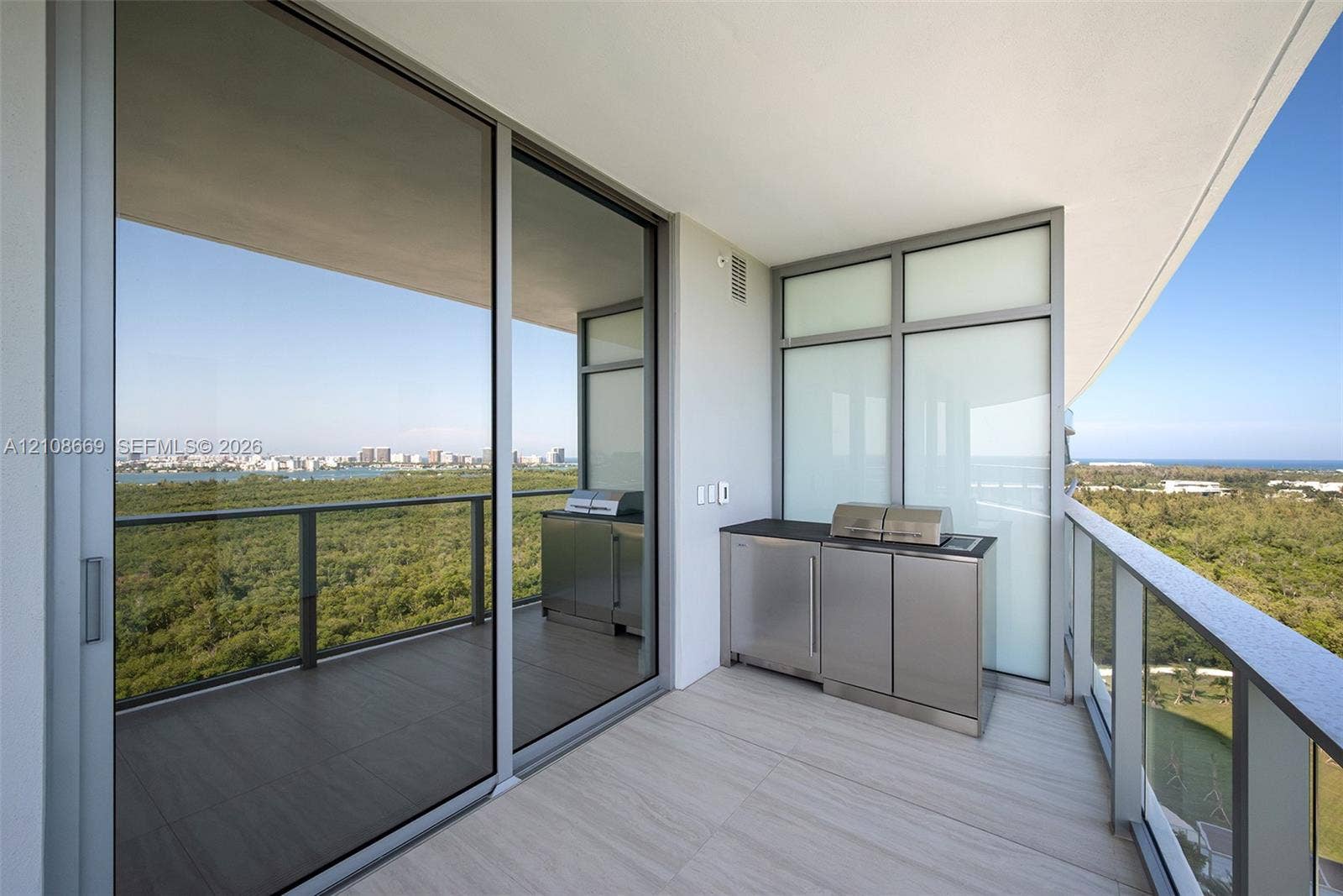 Covered balcony featuring tile flooring, metal railing, built-in stainless steel outdoor kitchen cabinetry, and expansive glass sliding doors