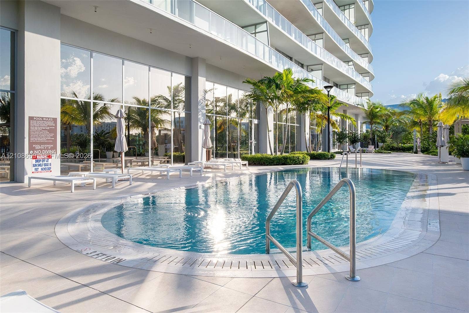 Swimming pool with stainless steel railings, light-colored tile decking, and floor-to-ceiling exterior glazing