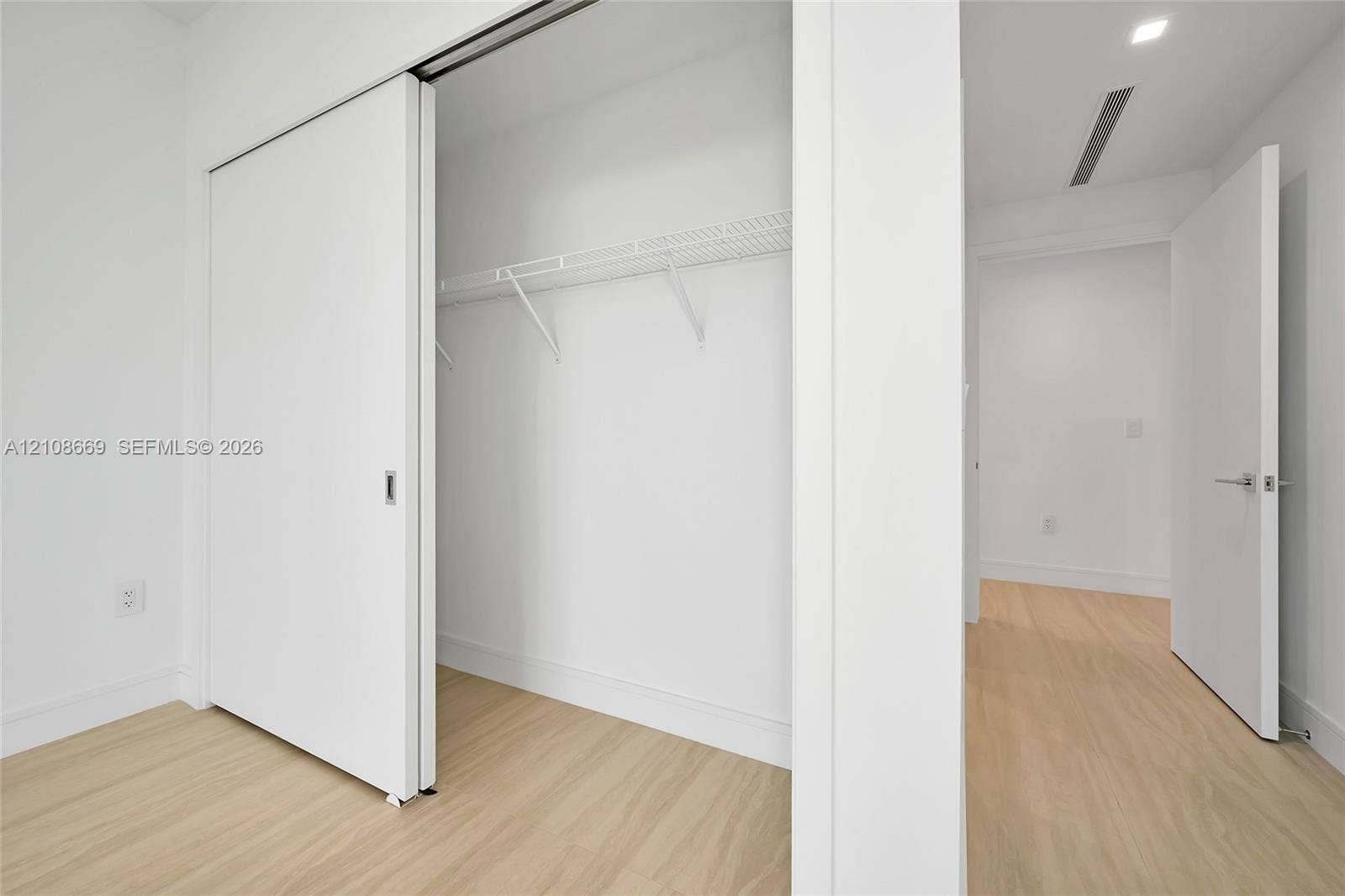 Sliding panel closet doors, white wire shelving, wood-finish flooring, and solid-core interior doors with satin nickel hardware