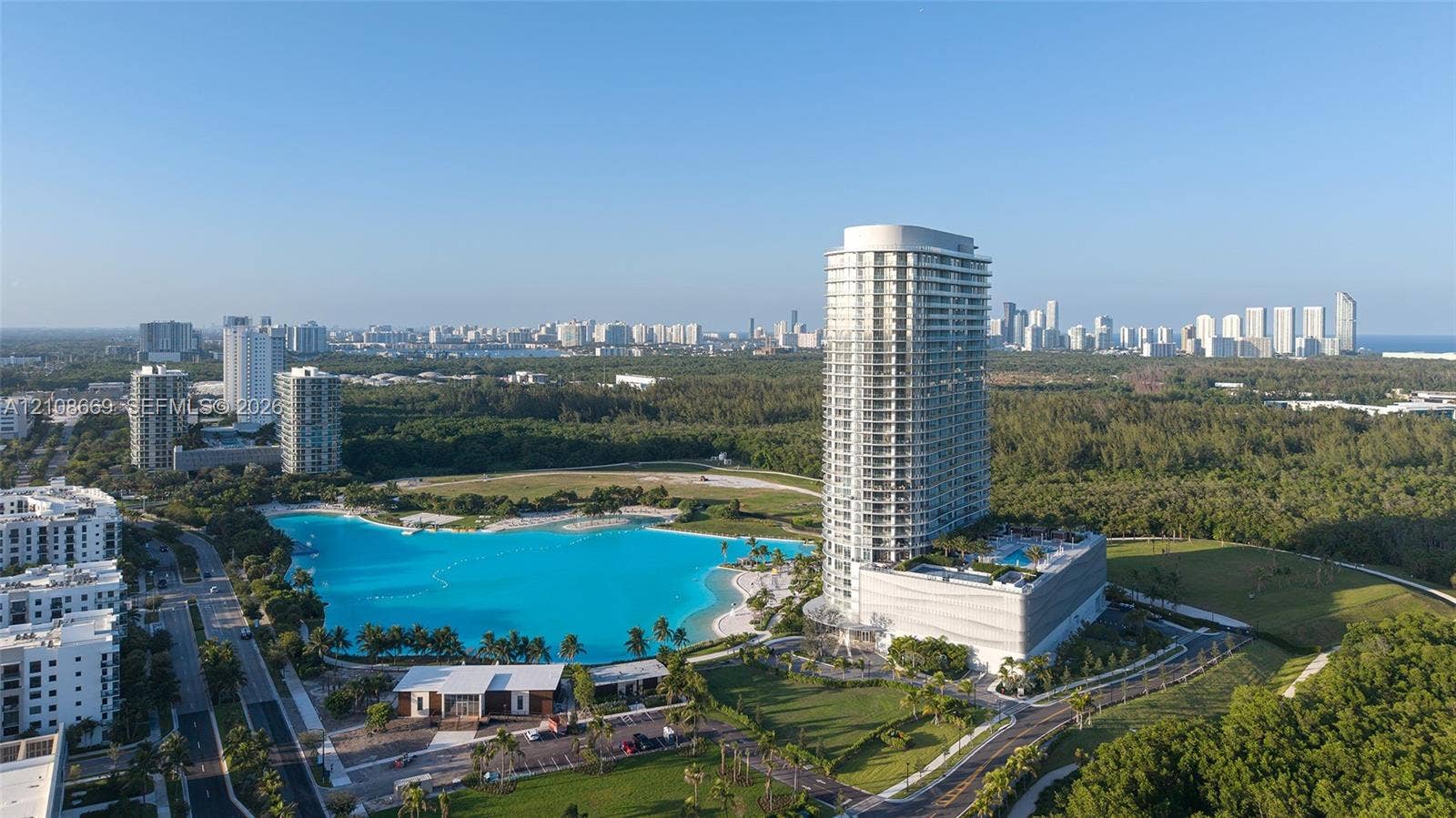 High-rise residential tower featuring a multi-story parking structure, private outdoor swimming pool, and proximity to a large-scale recreational lagoon