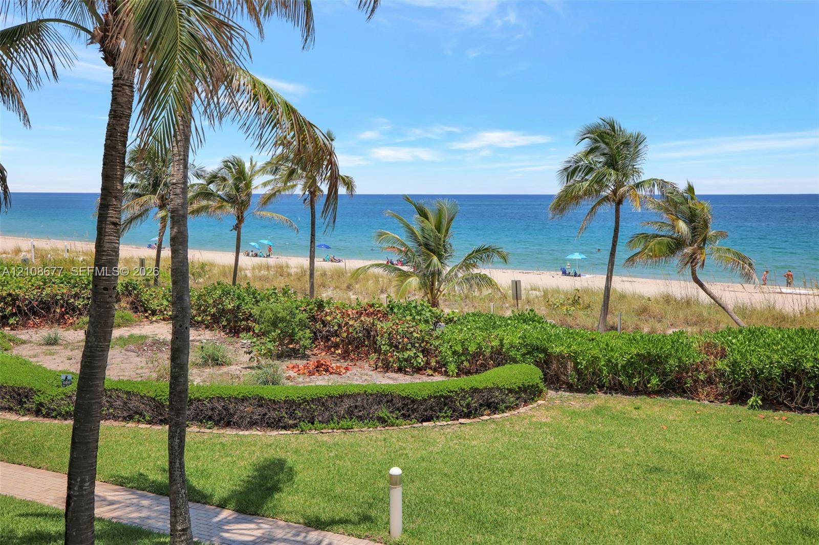 1440 S Ocean Boulevard, #11A, Lauderdale By The Sea, FL 33062 Oceanfront grounds featuring a landscaped lawn, groomed hedges, mature palm trees, and a stone-paver walkway