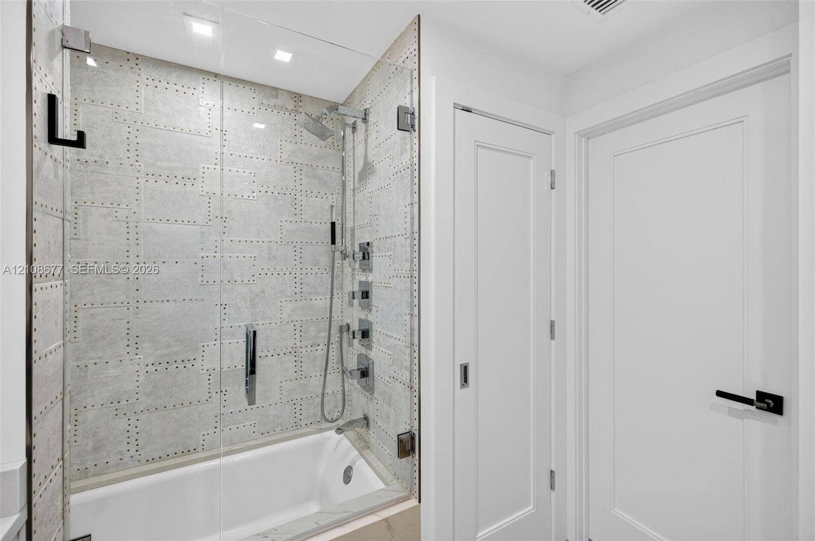 1440 S Ocean Boulevard, #11A, Lauderdale By The Sea, FL 33062 Shower enclosure featuring luxury patterned wall tile, frameless glass door, adjustable-height handheld showerhead, wall-mounted faucet controls, and recessed ceiling lighting plus linen closet