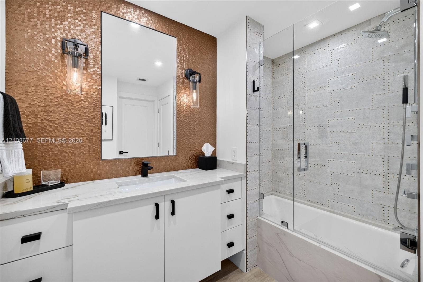 1440 S Ocean Boulevard, #11A, Lauderdale By The Sea, FL 33062 Bathroom featuring a hammered metallic tile accent wall, white floating vanity with stone counters, undermount sink, frameless glass shower enclosure, and custom decorative wall tile. Tub / shower combo w/ handheld shower head & rain head