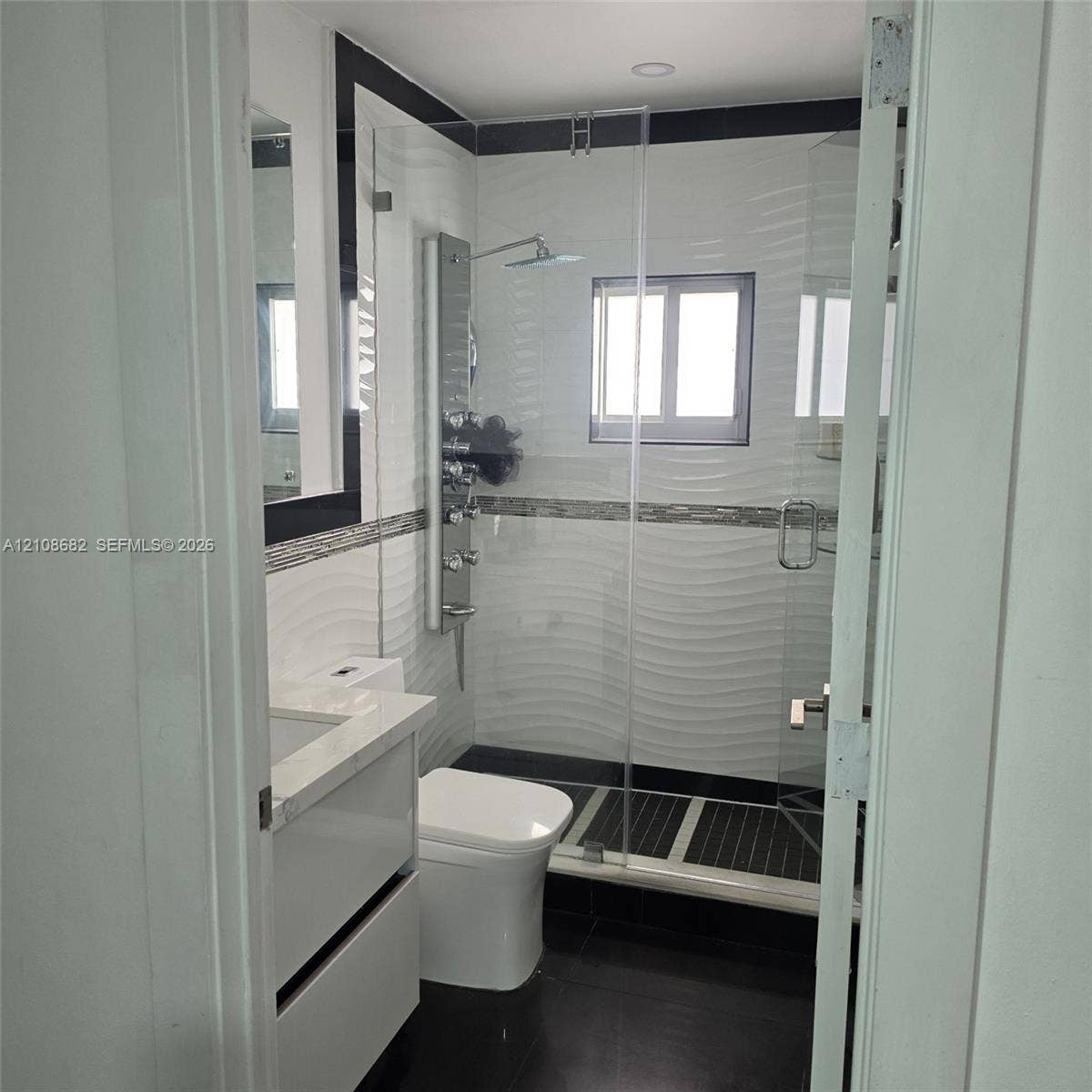 8943 NW 112th Terrace, Hialeah Gardens, FL 33018 Bathroom featuring a wall-mounted shower panel system, glass shower enclosure, vanity with a stone-top counter, textured tile wall accents, and dark floor tiling