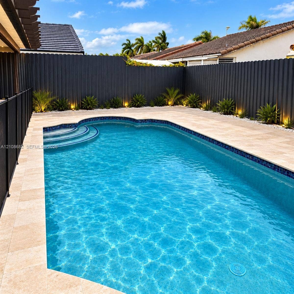 8943 NW 112th Terrace, Hialeah Gardens, FL 33018 In-ground swimming pool with integrated steps, surrounded by stone paver decking, enclosed by a corrugated metal privacy fence, and featuring perimeter landscape lighting