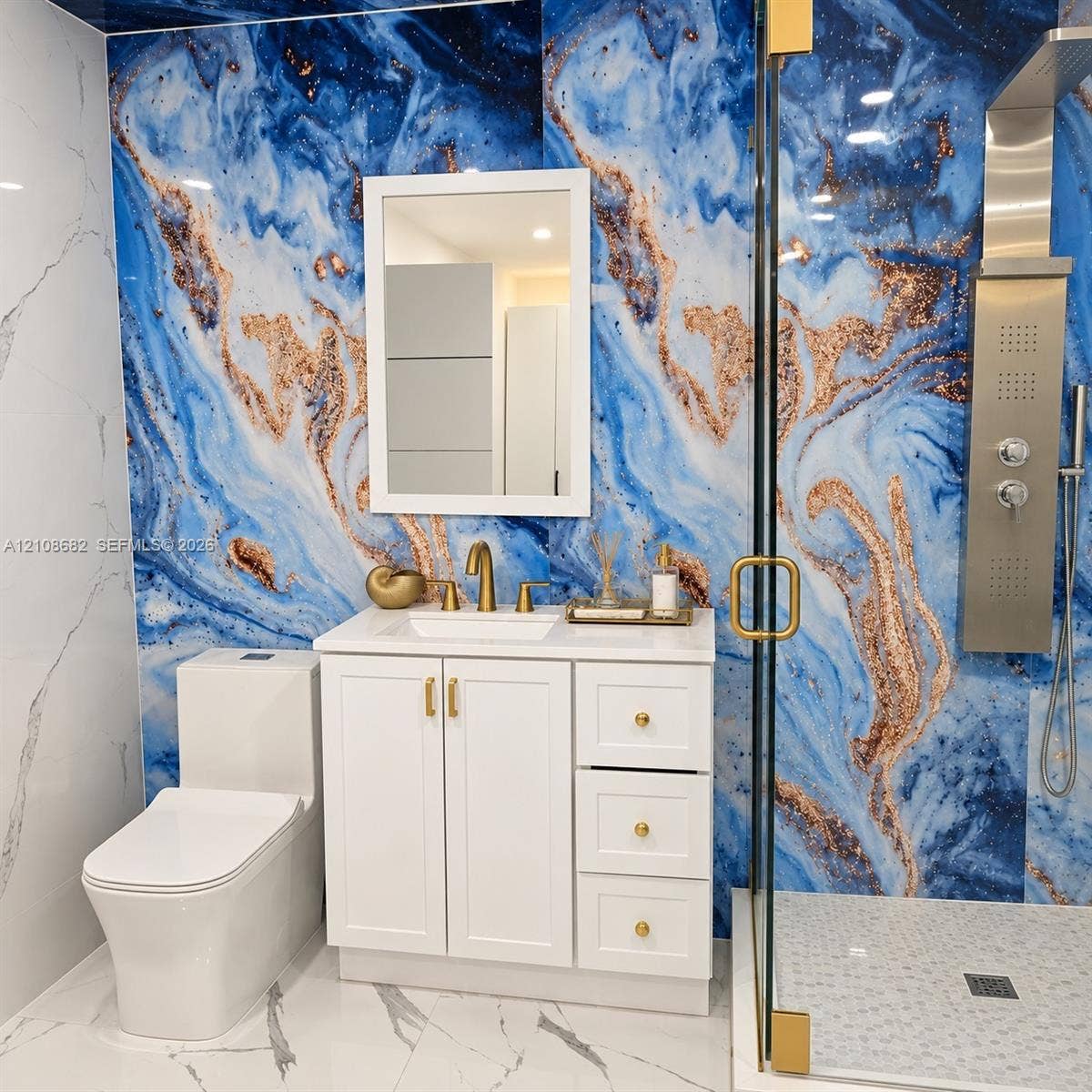8943 NW 112th Terrace, Hialeah Gardens, FL 33018 Bathroom featuring high-contrast blue and copper-toned wall paneling, white vanity with gold-finish hardware, rectangular under-mount sink, and a glass-enclosed shower with a metallic multi-function shower panel