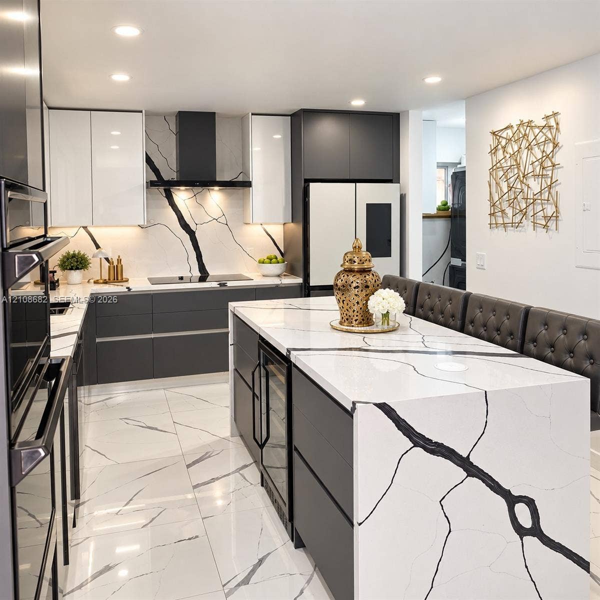 8943 NW 112th Terrace, Hialeah Gardens, FL 33018 Contemporary kitchen featuring a waterfall-edge island with stone-finish surfaces, dual-tone cabinetry, a matching stone-finish full-height backsplash, recessed lighting, and an integrated wine refrigerator