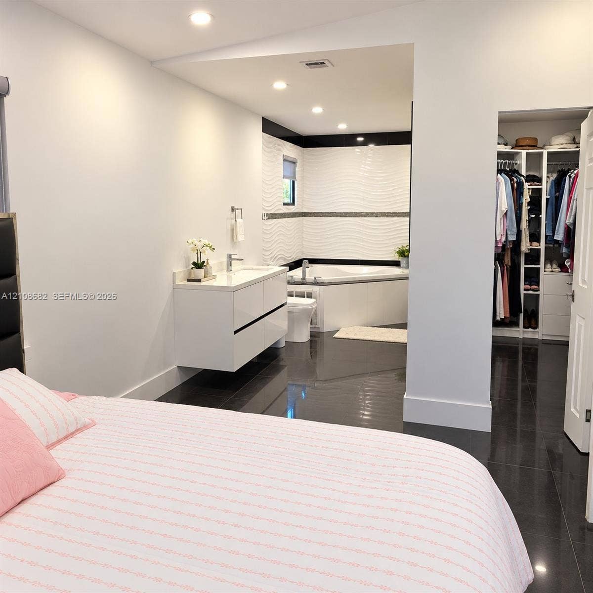 8943 NW 112th Terrace, Hialeah Gardens, FL 33018 Glossy tile flooring, wall-mounted double-drawer vanity with white countertop, soaking tub with textured tile surround, and walk-in closet featuring custom built-in shelving and organizers